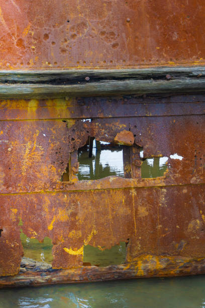 Derelict wooden fishing boat moored on the bank of the Tha Chin river in Bangkok, Thailand. Holes in the hole, broken, worn wood. Blue sky and clouds in the background.