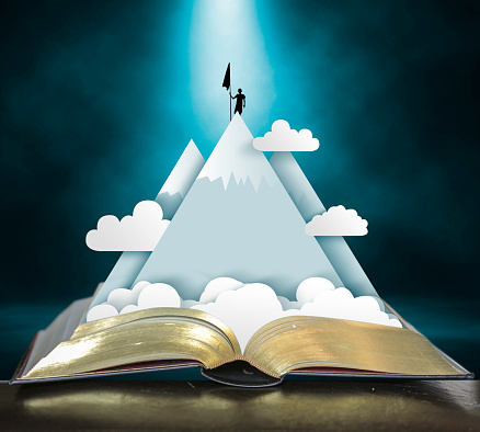 Open storybook with pop up of mountains, clouds and climber claiming the peak