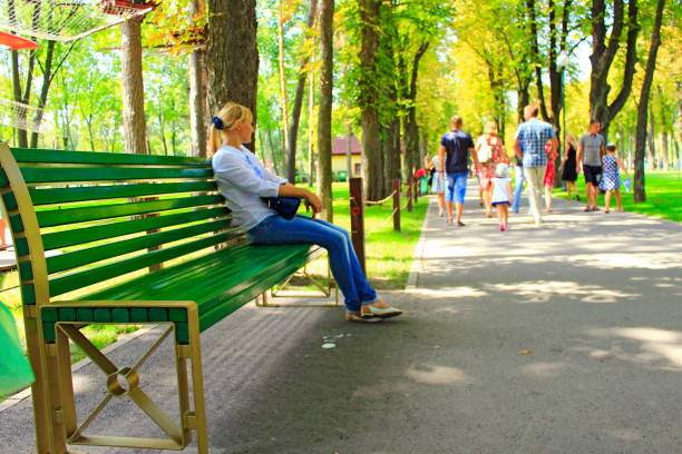 молодая женщина сидит на скамейке в красивом парке со многими зелеными деревьями - 11927 стоковые фото и изображения