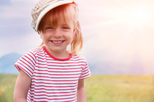 Child on vacation wearing green t-shirt hat and sunglasses over white isolated background picking up the hat.Kid with happy face smiling and looking at the camera. Positive person