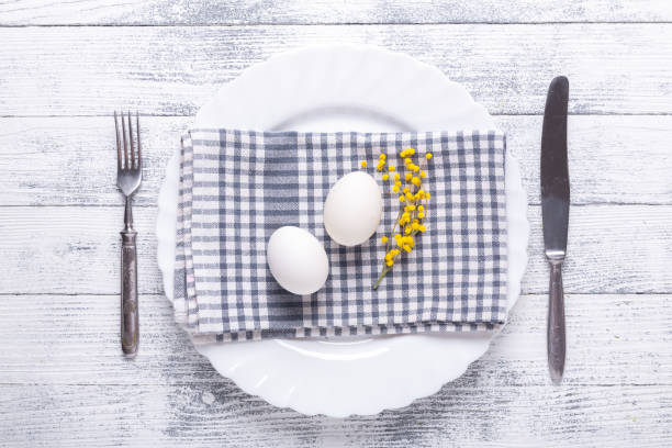 istock Easter table setting. White eggs, napkin on a plate, mimosa flowers, fork, knife on a wooden table 1139148642