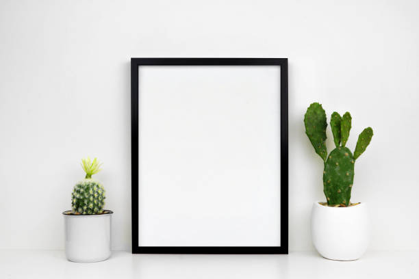 istock Mock up black frame with cactus plants on a white shelf or desk against a white wall 1139150383