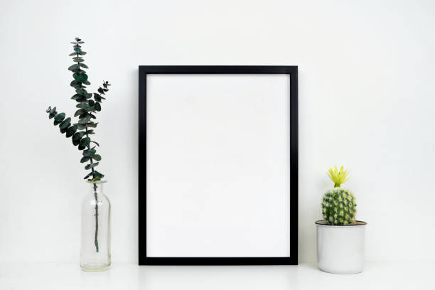 istock Mock up black frame with cactus and branches on a white shelf or desk against a white wall 1139150401