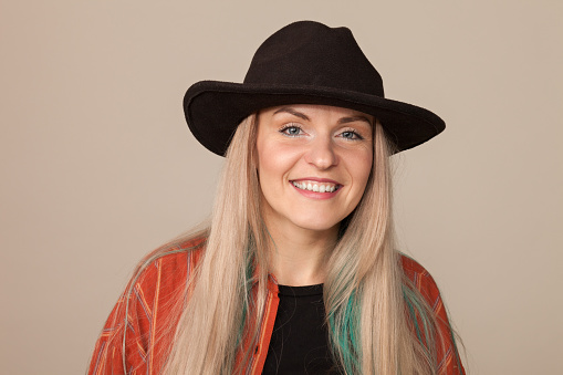 Studio portrait of an attractive 30 year old blonde woman in a black hat on a beige background