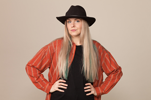 Studio portrait of an attractive 30 year old blonde woman in a black hat on a beige background