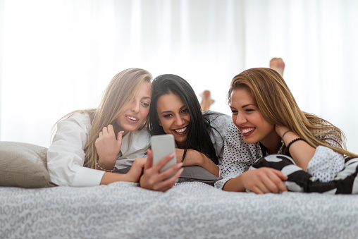 Three women having fun taking pictures on the bed with mobile phone.