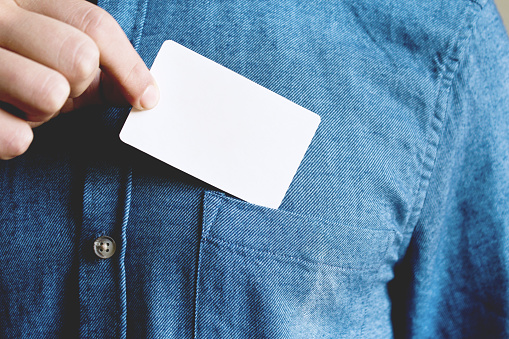 Young man is taking a blank card in the pocket of his shirt. Close up.