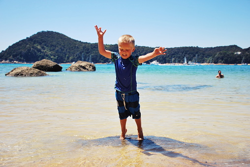 A young boy leaps off the rocks into the sea. This image is taken at Anchorage Beach in the Abel Tasman National Park in the Tasman District of New Zealand's South Island.