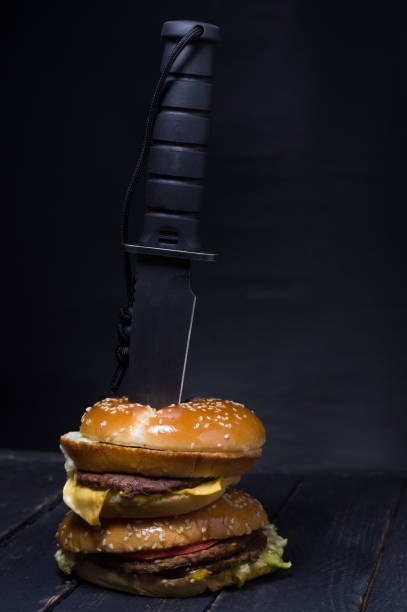 Black big knife inserted into a burger. Black background.