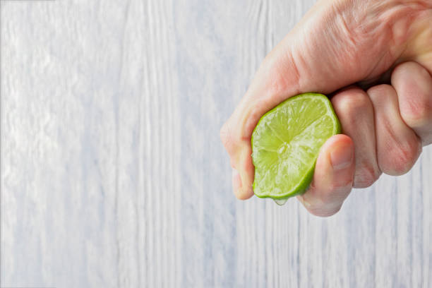 la mano di un uomo spreme il succo da una fetta di lime metà. succosa goccia appesa. - mature women isolated mature adult women foto e immagini stock