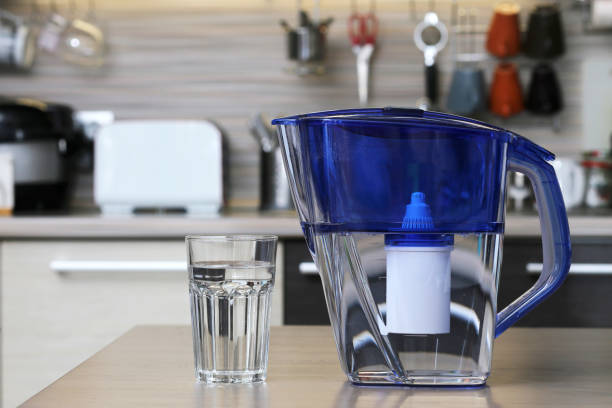 Glass of clean water and filter for cleaning drinking water on the table in the kitchen. Purification of drinking water at home Glass of clean water and filter for cleaning drinking water on the table in the kitchen. Purification of drinking water at home pitcher jug stock pictures, royalty-free photos & images