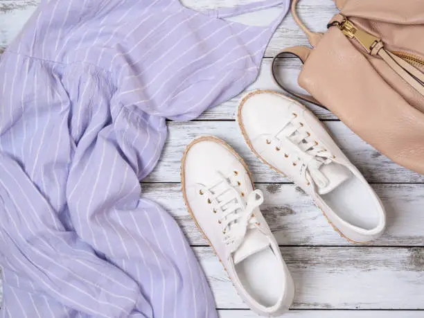 Photo of Womens clothing, shoes, accessories (lavender dress, white leather sneakers, beige backpack). Fashion outfit, spring summer collection. Shopping concept. Flat lay, view from above