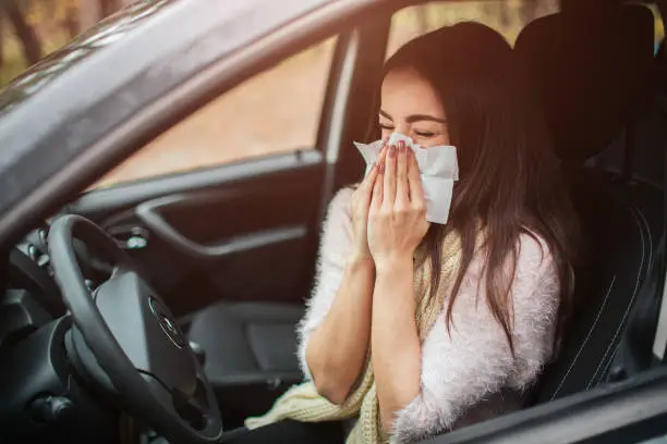 Photo of young woman with handkerchief. Sick girl has runny nose. female model makes a cure for the common cold in the car