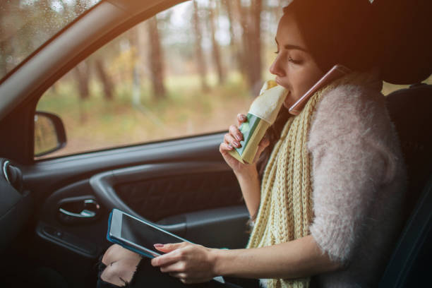 la donna impegnata ha fretta, non ha tempo, mangerà uno spuntino in movimento. lavoratore che mangia e parla al telefono allo stesso tempo. ha multitasking mentre mangia e lavora su un tablet pc - driving mobile phone car talking foto e immagini stock