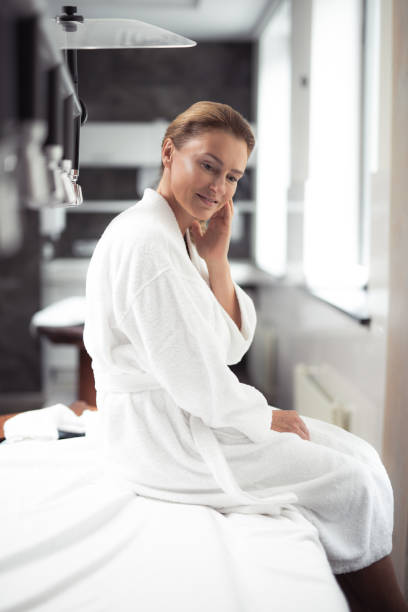 istock Charming middle aged woman in bathrobe sitting on massage table at spa salon 1139182835