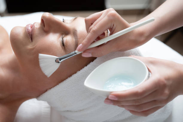 istock Beautician using cosmetic brush for applying mask on lady cheek 1139182854