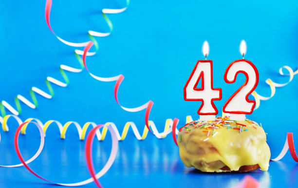 Birthday of forty two years. Cupcake with white burning candle in the form of number 42. Vivid blue background with copy space Birthday of forty two years. Cupcake with white burning candle in the form of number 42. Vivid blue background with copy space number 42 stock pictures, royalty-free photos & images