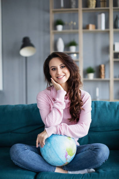 istock Smiling woman with globe sitting on a sofa at home. 1139212429