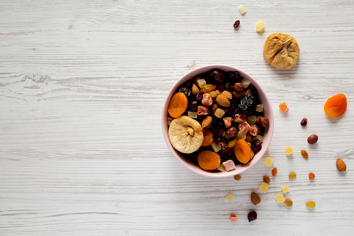 Dried fruits and nut mix in a pink bowl on white wooden background, top view. Overhead, from above, overhead. Copy space.