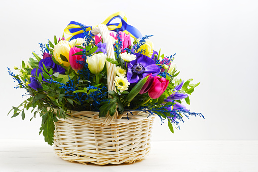 Bouquet of flowers in a wicker basket on white wooden table
