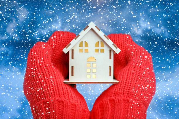 istock Hands in knitted mittens Holding model House on snowfall background. 1139242532