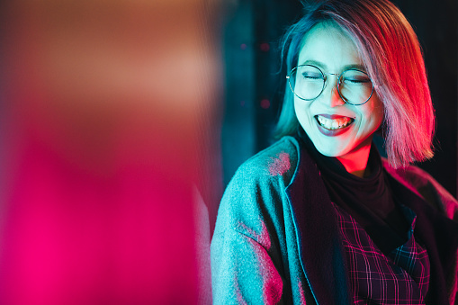 A portrait of a young and happy woman lit up by neon lights.