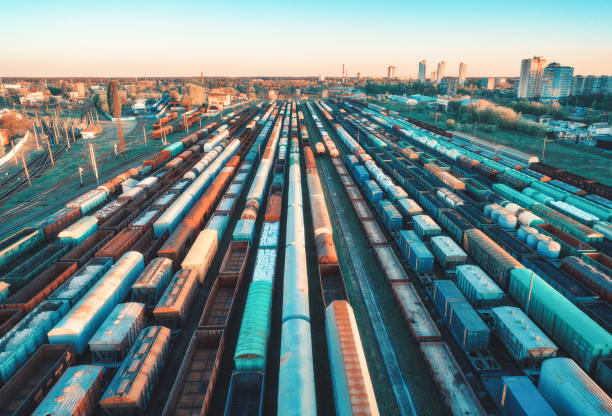 vue aérienne des trains de marchandises colorés sur la gare au coucher du soleil. wagons avec marchandises sur le chemin de fer. industrie lourde. scène industrielle avec des trains de fret, des bâtiments urbains. vue de dessus du drone. vintage - railroad track railroad station platform transportation freight transportation photos et images de collection