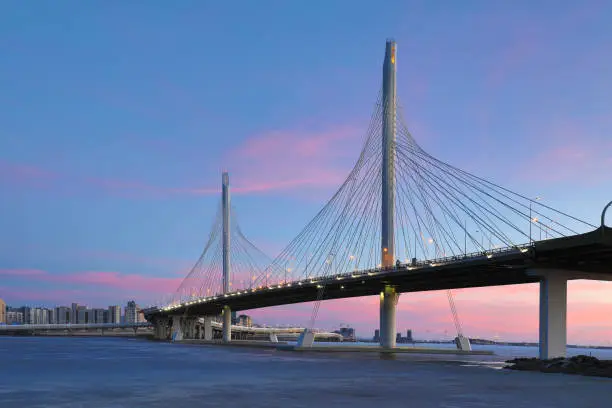 Photo of The bridge of circle highway road over Neva river near the mouth of it in the blue hour after the sunset. Night view on the buildings of Petersburg city and the Finish gulf