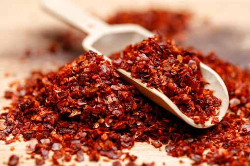 Dried ground red pepper and seeds on wooden background