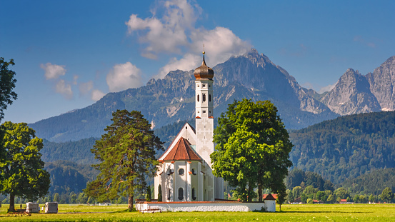 Bavarian landscape - view of the church of St. Coloman on the background of the Alpine mountains