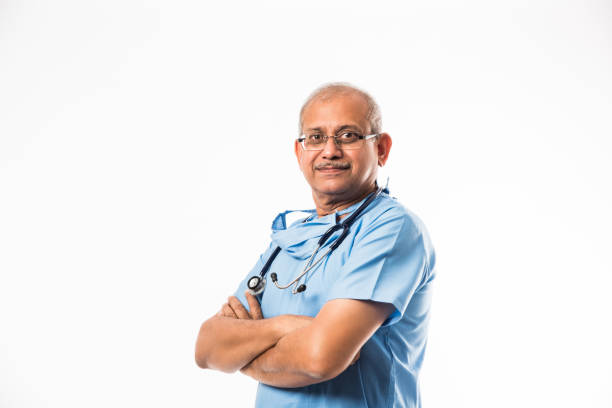 hochrangiger indischer männlicher chirurg in blauem kleid, stehend mit stethoskop über weißem hintergrund - portrait black and white senior men wisdom stock-fotos und bilder