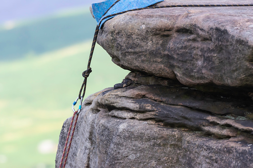 Two ropes connected with carabiner hanging from cliff edge. Anchor point with cloth placed between rope and abrasive rock to protect it from friction.Climbing equipment in use.