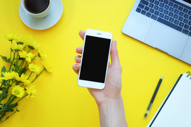 istock Womans hand holding a phone at the table office. Yellow background 1139269612