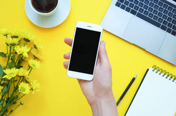 istock Womans hand holding a phone at the table office. Yellow background 1139269662