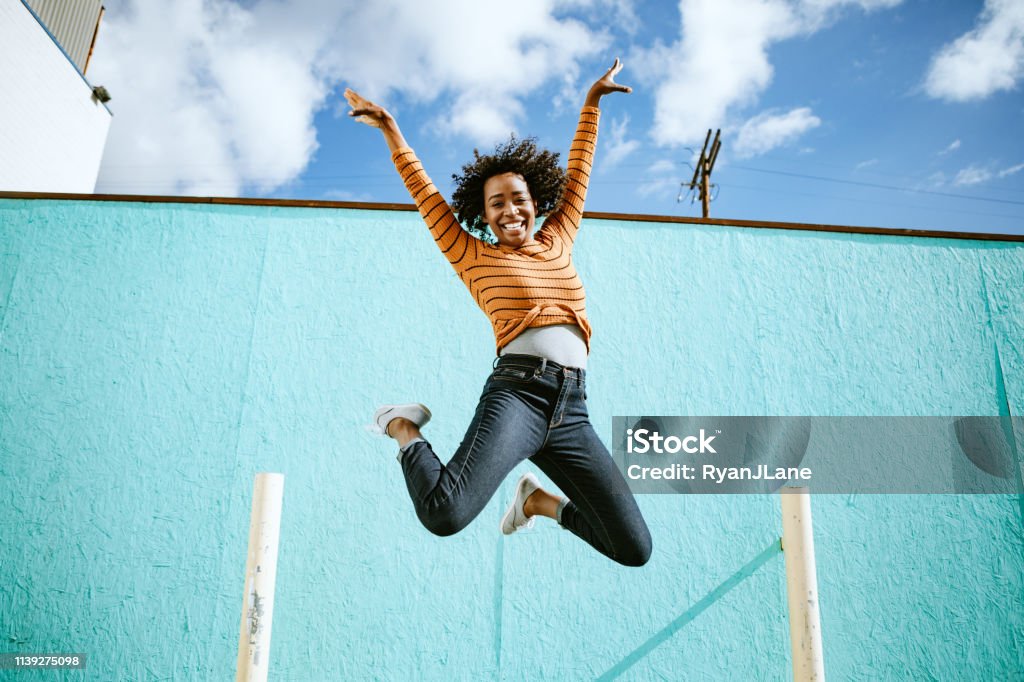 Celebrating Woman Jumps Into The Air A beautiful African American woman smiles, jumping high in the air with her arms outstretched and a smile on her face.  Horizontal image with copy space.  Shot in Los Angeles, California. Jumping Stock Photo