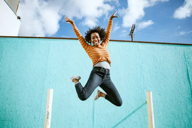 A beautiful African American woman smiles, jumping high in the air with her arms outstretched and a smile on her face.  Horizontal image with copy space.  Shot in Los Angeles, California.