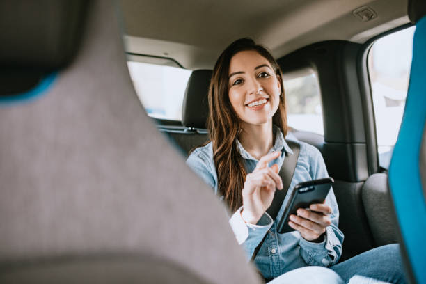Woman In Car Rideshare In City of Los Angeles A Latina business woman rides in a crowdsourced taxi, having requested a pick up and drop off on her smartphone.  Shot in Los Angeles, California. car pooling stock pictures, royalty-free photos & images