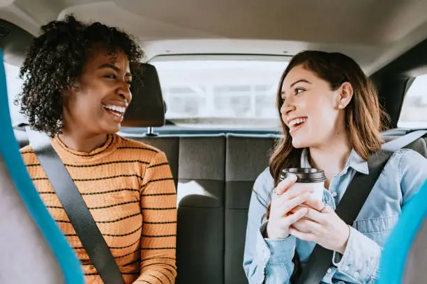 Two friends ride in a crowdsourced taxi, having requested a pick up and drop off on a smartphone.  Shot in Los Angeles, California.