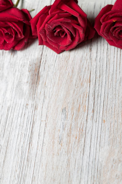 istock Three Red roses on light wooden background with copy space, top view, vertical composition  - Image 1139276365