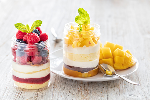 Raspberry and mango dessert, cheesecake, trifle, mouse in a glass jar on a light wooden background