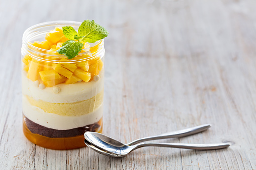 Sweet homemade Mango dessert, cheesecake, trifle, mouse in a glass jar on a light wooden background with copy space