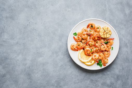 Roasted shrimps with lemon, garlic and herbs. Seafood, shelfish. Shrimps Prawns sauteed with spices, garlic and lemon on gray background, copy space. Shrimps prawns on plate.