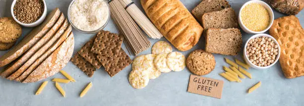 Gluten free food. Various gluten free pasta, bread, snacks and flour on light gray background, top view, banner.