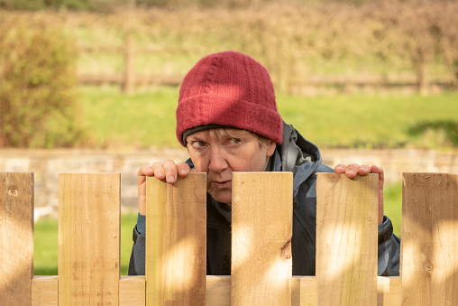 Mature woman hiding behind fence outdoors