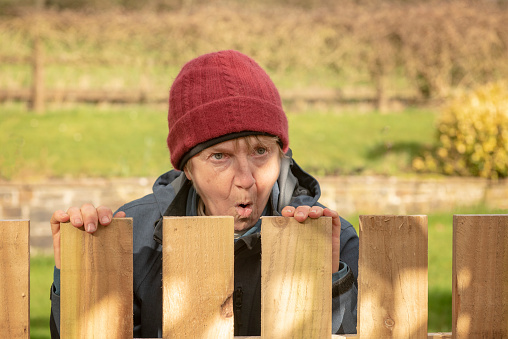 Shocked mature woman looking over fence outdoors