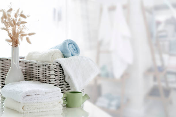 Stock photo showing close-up view of pile of folded, white towels being carried by an unrecognisable person to put on high shelf in a luxury hotel bathroom with horizontal stacked pattern, white bevelled edged wall tiles. Home furnishings and bedroom interior design.