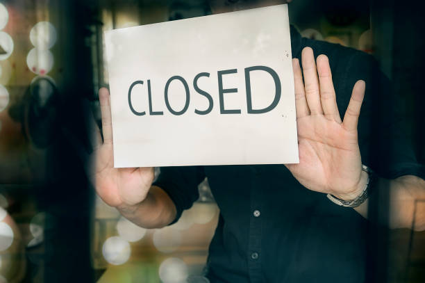 man putting closed sign in window in shop. late at night in city. - business closed imagens e fotografias de stock