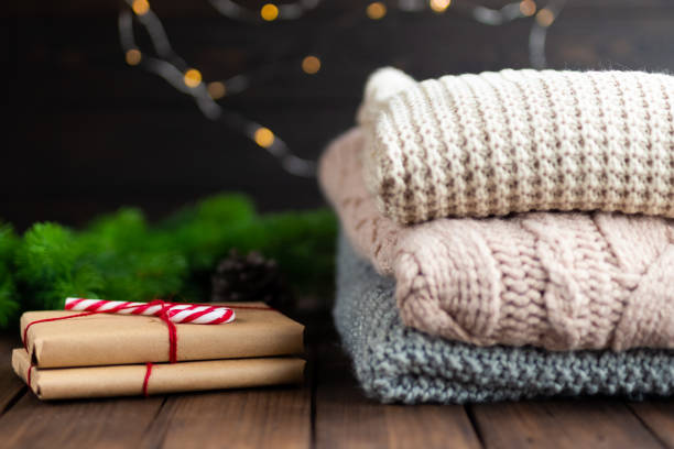 Stos swetrów z wełny alpaki obok zapakowanych prezentów na drewnianej powierzchni, przywołujący ciepło i luksus.