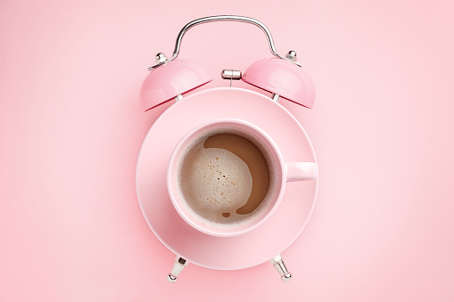 Pink alarm clock and coffee cup on pink background. Breakfast time concept. Minimal style