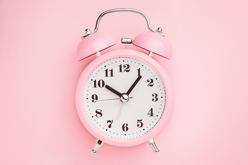 Pink alarm clock on pink background. Minimal style
